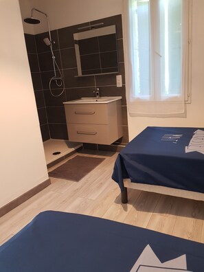 Un dormitorio con cama, una mesita de noche, ventana con cortinas, baño con ducha, lavamanos y espejo.