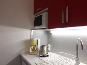 Cozinha com micro-ondas, cafeteira, chaleira e uma cesta de arame no balcão.