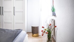 A bedroom with a bed, a bedside table, a small stool, a radiator, and a wall-mounted shelf with a plant. - House Felix Weinbergblick (Radebeul)