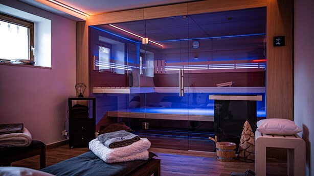 A modern spa room with a glass-enclosed sauna, wooden flooring, and a bench with towels. - House Felix Weinbergblick (Radebeul)