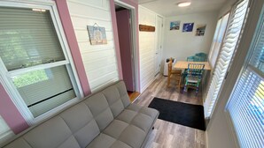 Un salon avec un canapé beige, une table à manger avec des chaises, et un coin cuisine visible à travers une porte ouverte.