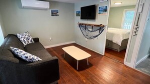 Un salon avec un canapé, une petite table, un hamac et un téléviseur fixé au mur.