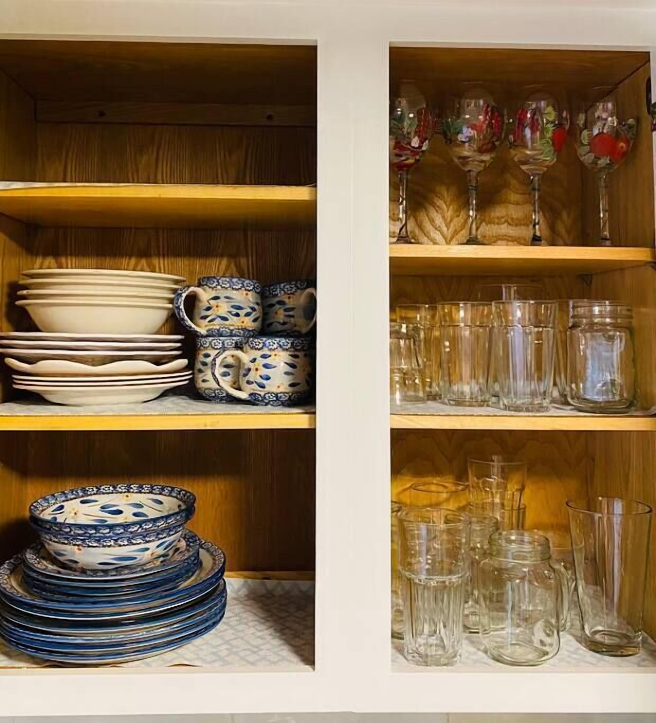 Un armario de cocina con repisas que contienen platos, tazas y cristalería.