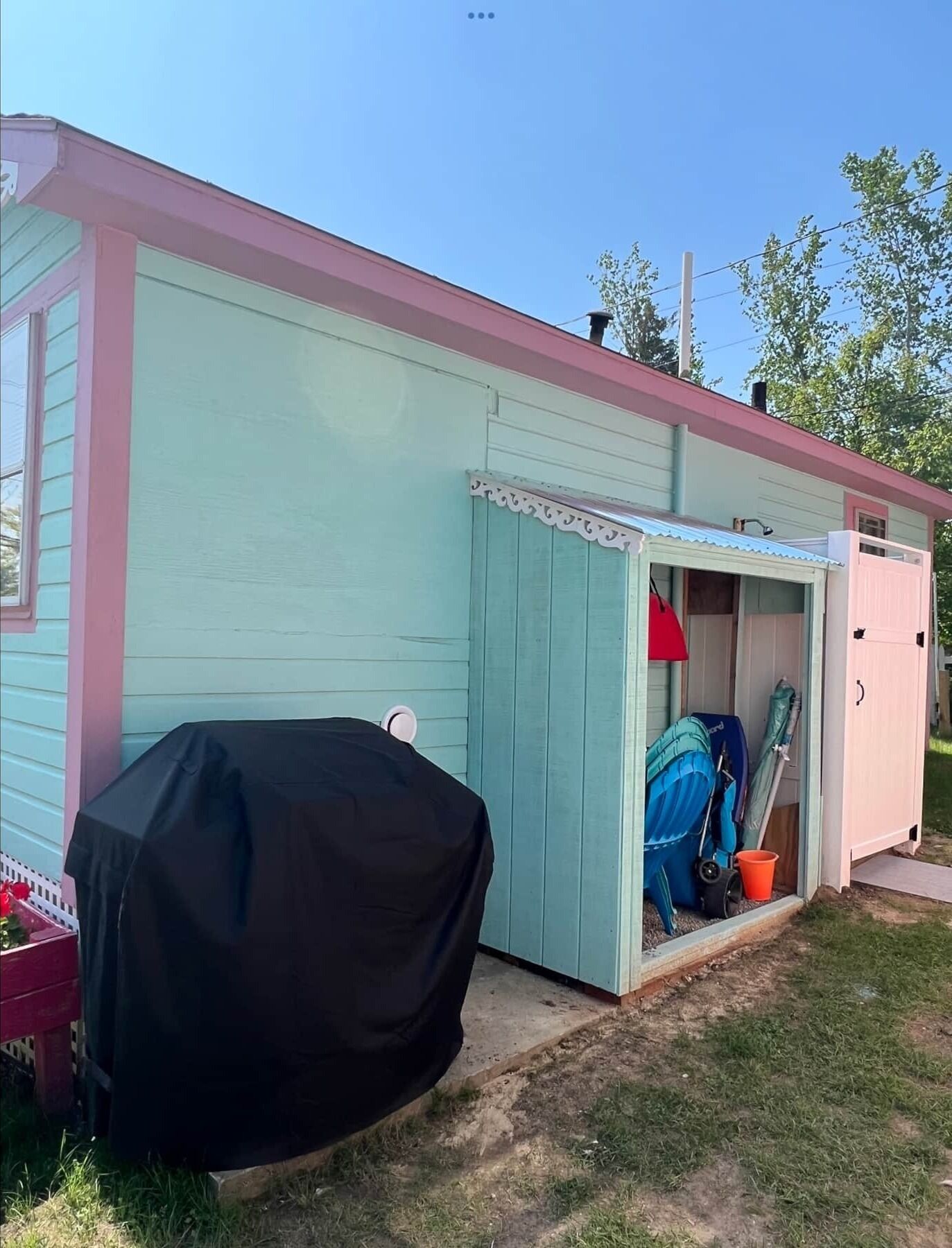 A small shed with a blue exterior and a white door. Inside, there is a blue folding chair, a red lamp, and a white cabinet.