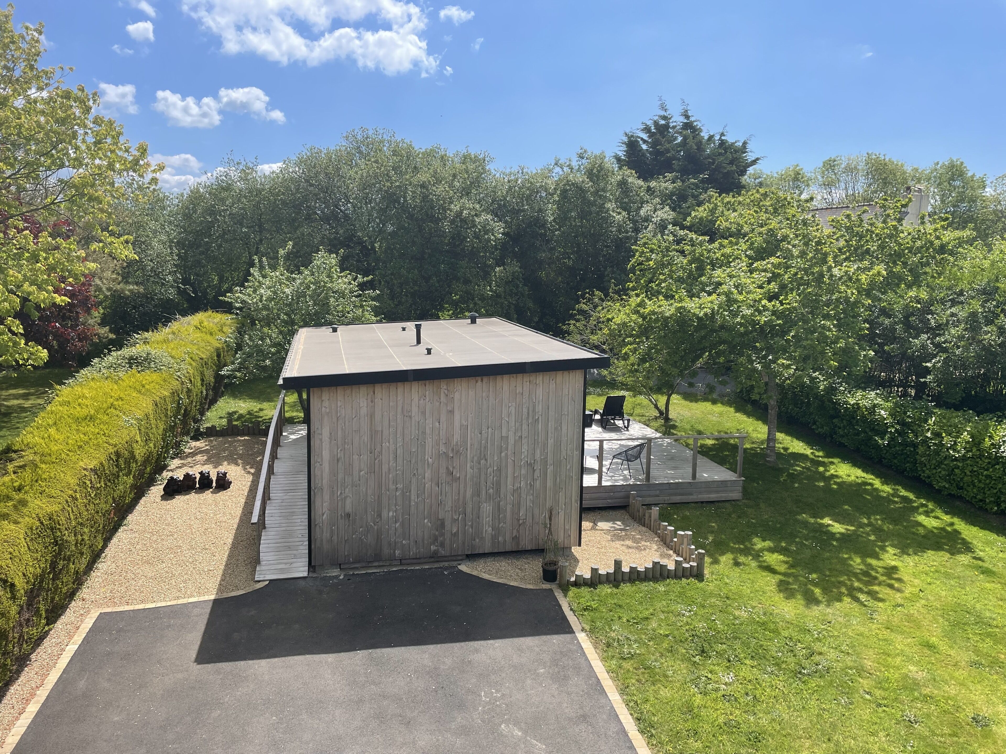 A wooden structure with a flat roof, a deck with chairs, and a paved area in front.