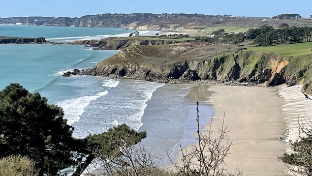 Un paisaje costero con una playa, acantilados y un pueblo distante.
