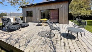 Una terraza moderna al aire libre con piso de madera, sillas metálicas y una mesa amarilla.