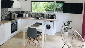 Una cocina moderna con horno empotrado, microondas y lavadora, un comedor con mesa y sillas, y un ventanal con vistas al verdor.