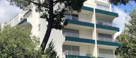 Un immeuble à plusieurs étages doté de balcons, entouré d’arbres.