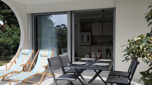 Ein moderner Essbereich im Freien mit Tisch und Stühlen, eine überdachte Sitzgruppe mit Liegestühlen und Blick ins Haus.