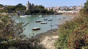 Eine Küstenstadt mit einem historischen Turm und einer Kirche. Boote liegen an der Küste vor Anker.