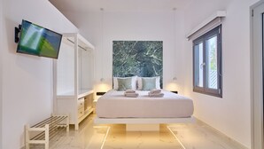 A modern bedroom with a large bed, a TV mounted on the wall, and a window providing a view of greenery.