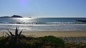 A beach with clear skies, calm water, and distant landforms.