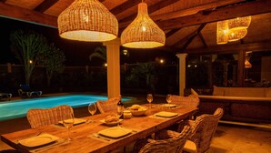 Un espace extérieur aménagé pour les repas, avec une piscine, des meubles en osier et des guirlandes lumineuses.