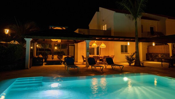 Un espace aménagé au bord de la piscine, comprenant des chaises longues, un coin repas et une terrasse couverte.