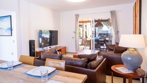 Un salon moderne comprenant un coin repas, des canapés en cuir, un téléviseur et une table mise pour deux personnes.