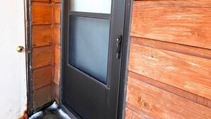 Eine Holztür mit schwarzem Rahmen und einem Glasfenster, eine Metall-Zahl '61' an der Wand und eine kleine Leuchte darüber.