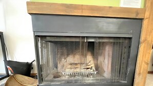 Ein Kamin mit einem Metallsieb, einem hölzernen Sims und einem schwarzen Fliesenboden.