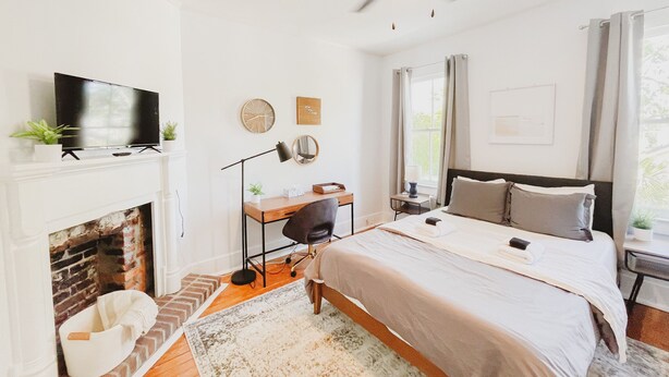 A bedroom with a bed, a desk, a television, a fireplace, and a ceiling fan. - Craftsman-style Starland District Gem ☆ Home Office & Back Yard ☆ Pet-Friendly (Savannah)