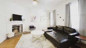 A modern living room with a black leather sofa, a white coffee table, a fireplace, and a flat-screen TV mounted on the wall. - Craftsman-style Starland District Gem ☆ Home Office & Back Yard ☆ Pet-Friendly (Savannah)