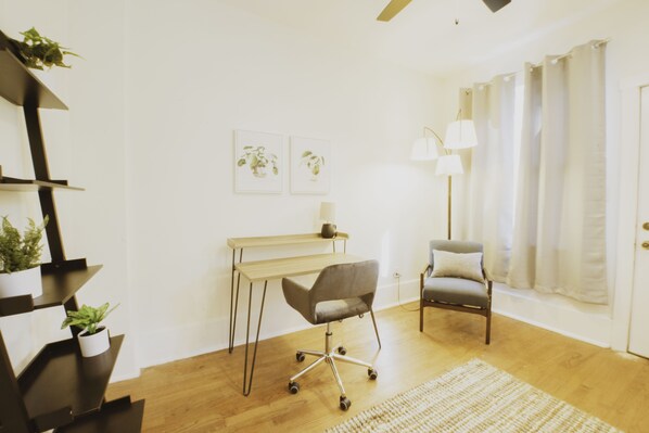 Una habitación moderna con suelo de madera, un escritorio con silla, una lámpara y dos cuadros colgados en la pared.