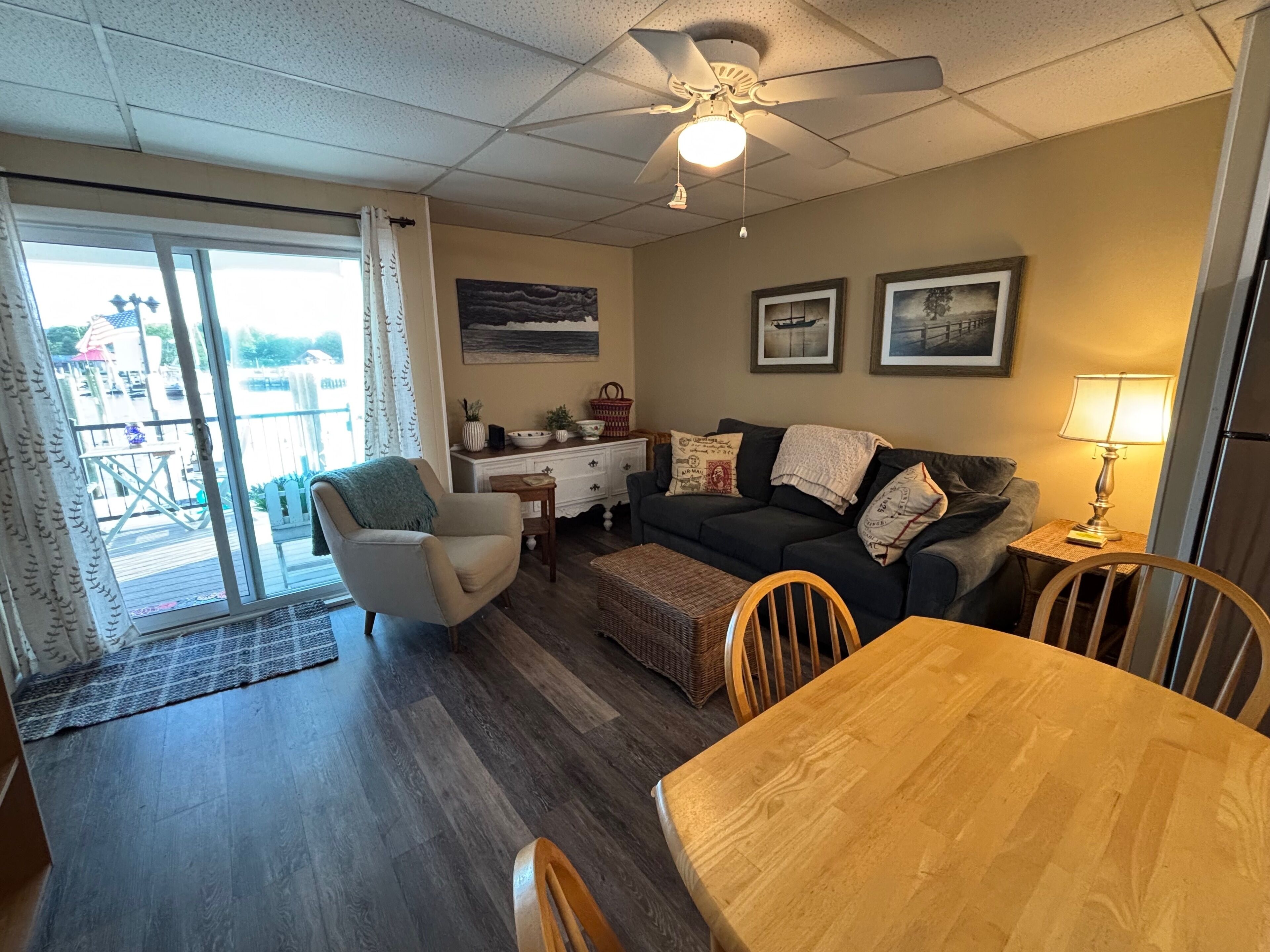 A living room with a sofa, armchairs, a wooden dining table, and a ceiling fan.