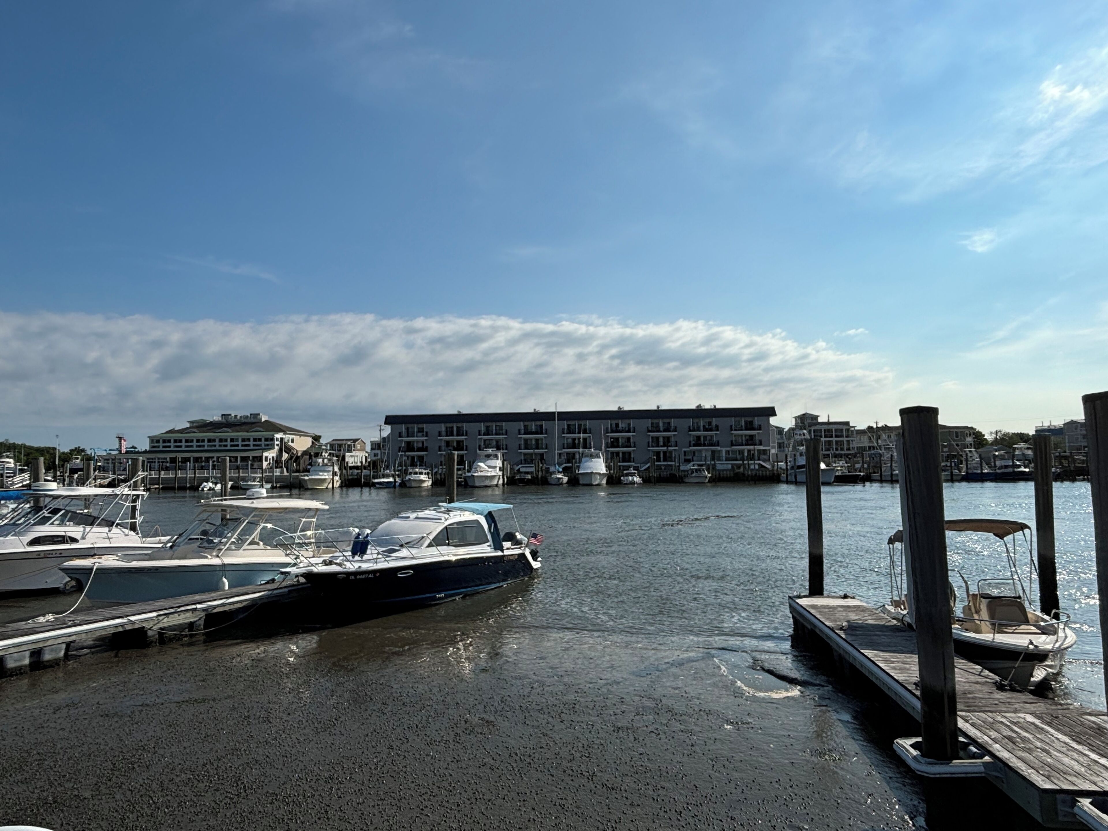 Een jachthaven met aangemeerde boten, een houten steiger en een gebouw met meerdere balkons in de verte.