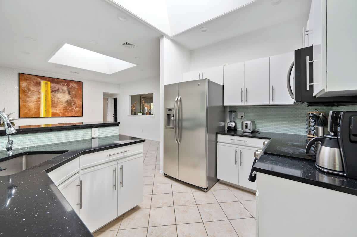 A modern kitchen with white cabinets, a stainless steel refrigerator, a black countertop, and a skylight.