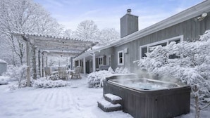 Un espace extérieur abrité comprenant un jacuzzi, une terrasse en bois et des arbres couverts de neige.