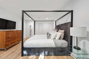 A modern bedroom with a bed, a TV, a dresser, and a glass side table. - Villa Luz Family Home w/ heated pool & jacuzzi (Hampon Bays)