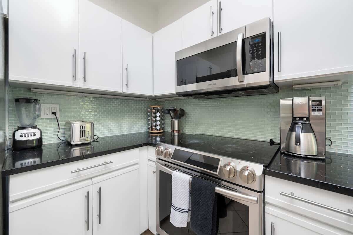 A modern kitchen with white cabinets, a black countertop, a stainless steel stove, a microwave, and a coffee maker.