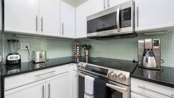 A modern kitchen with white cabinets, a black countertop, a stainless steel stove, a microwave, and a coffee maker.