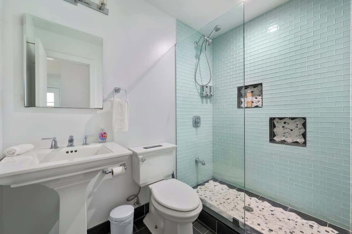 A bathroom with a white sink, mirror, and toilet. It has a glass-enclosed shower with a tiled wall.