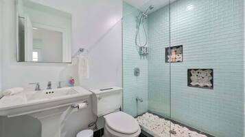 A bathroom with a white sink, mirror, and toilet. It has a glass-enclosed shower with a tiled wall.