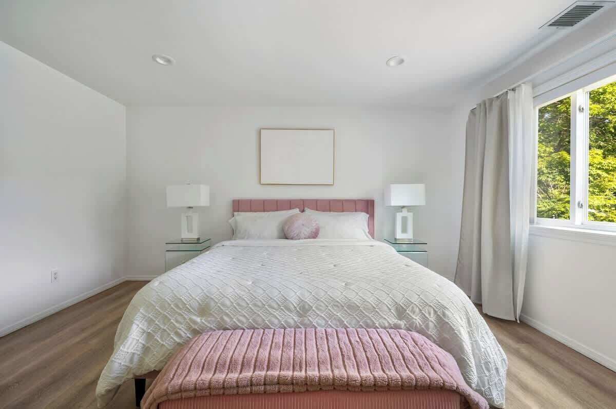 A bedroom with a bed, bedside tables, a window with curtains, and a framed picture on the wall.