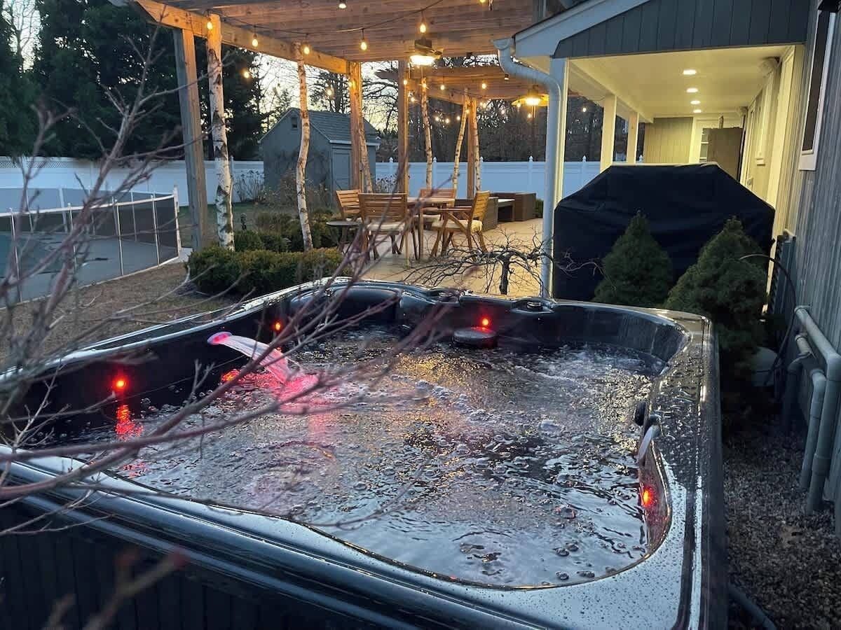 Un bain à remous dans un jardin, avec un patio couvert et un barbecue.