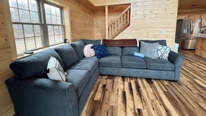 Interior moderno de una cabaña de troncos con un sofá modular, una escalera y una zona de cocina.