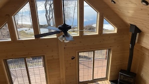 Una habitación con techos altos, ventanas amplias, ventilador de techo y estufa de leña.