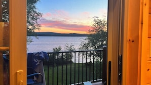 Una terraza de madera con un banco y una parrilla, con vistas a un lago y un atardecer.