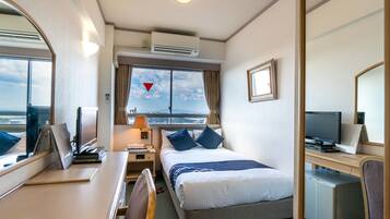 A hotel room with a bed, desk, chair, TV, and a view of the sea.