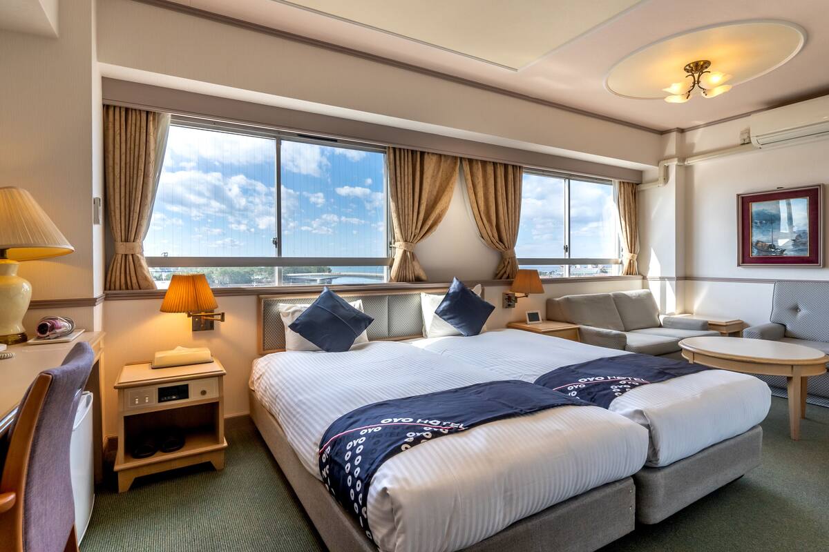 Ein Hotelzimmer mit einem großen Bett, zwei Nachttischen, einem Schreibtisch, einem Sessel und Blick ins Freie.