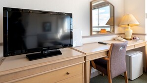 Habitación de hotel con televisión de pantalla plana, escritorio con lámpara, silla, refrigerador y espejo.