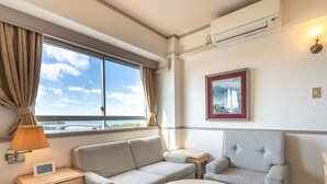 Habitación de hotel con sofá, una mesita, lámpara, un cuadro y vista al mar.