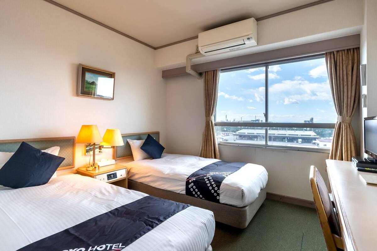 Ein Hotelzimmer mit zwei Betten, einem Schreibtisch, einem Stuhl, einer Klimaanlage, einem Fenster mit Blick und einer Lampe.
