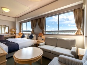 Een hotelkamer met twee bedden, een slaapbank, een ronde tafel en een bureau met lampen.