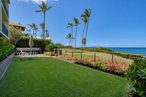 A well-maintained lawn with a seating area, palm trees, and a view of the ocean.