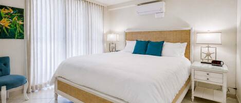 A hotel room with a large bed, two bedside tables with lamps, a ceiling fan, and an air conditioning unit.