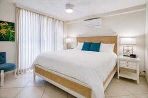 A hotel room with a large bed, two bedside tables with lamps, a ceiling fan, and an air conditioning unit. - Punahoa Beach 201 - Direct Ocean Front, Beautiful Renovation, Split AC, Wi-Fi (Kihei)