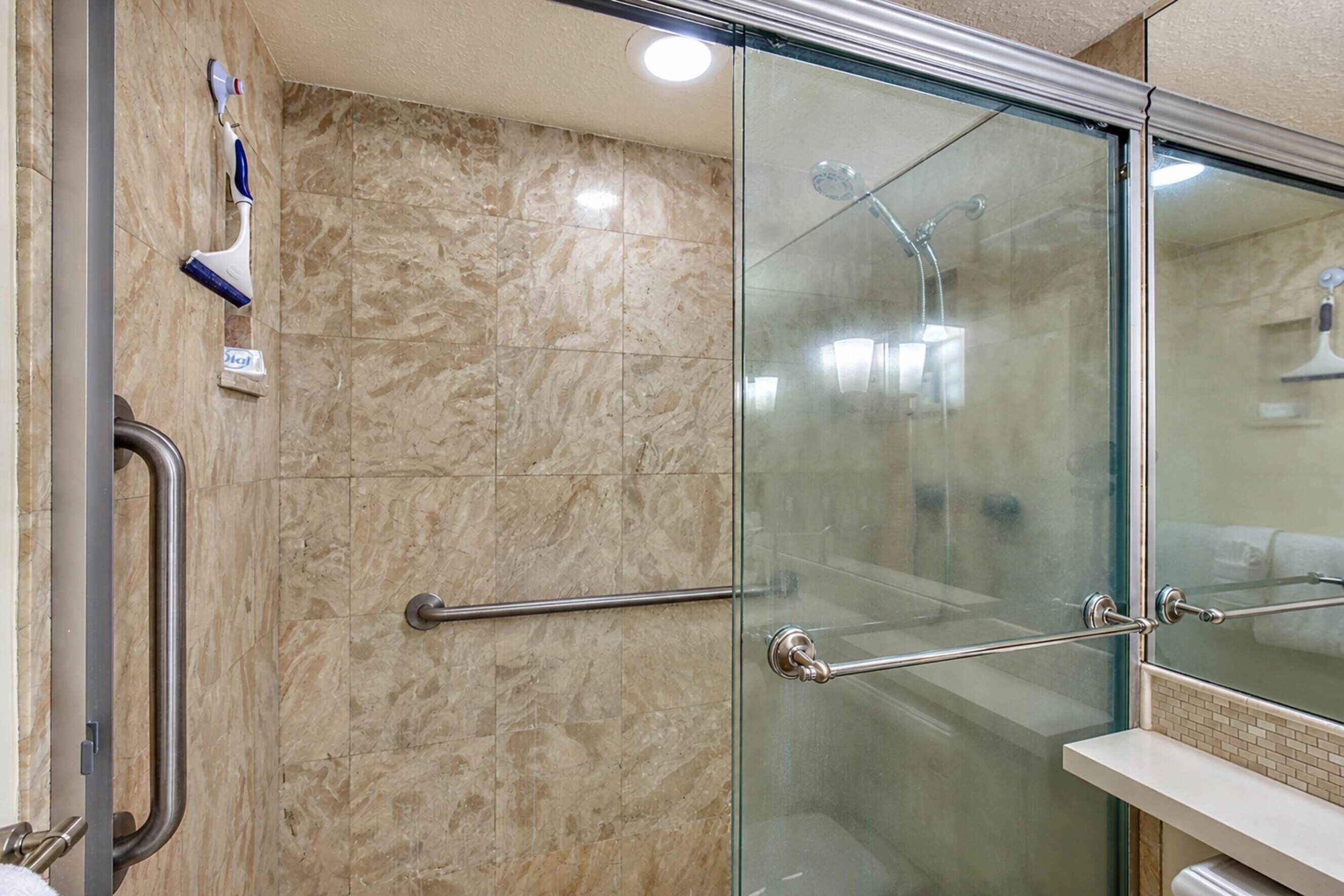 A modern bathroom with a glass shower enclosure, marble tiles, and a handrail.