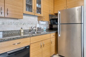 A modern kitchen with wooden cabinets, a stainless steel refrigerator, a granite countertop, and a built-in dishwasher.